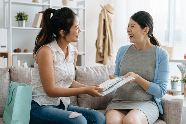 Two women sitting on a couch, one is hanging the other a gift.