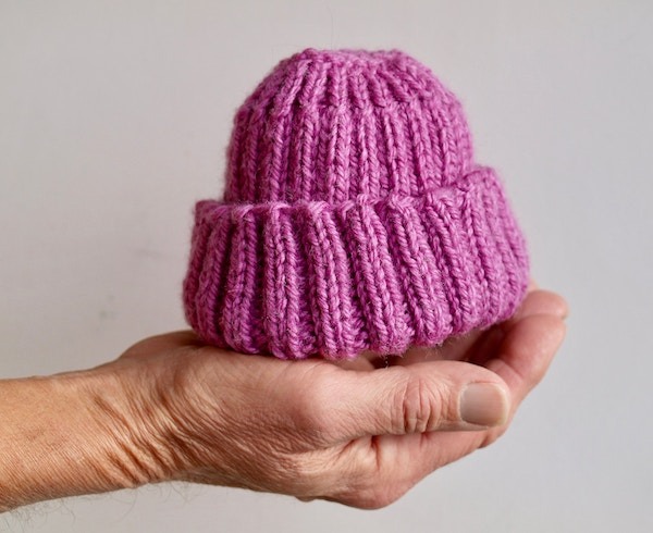 A pink knitted baby hat for a doula to gift.